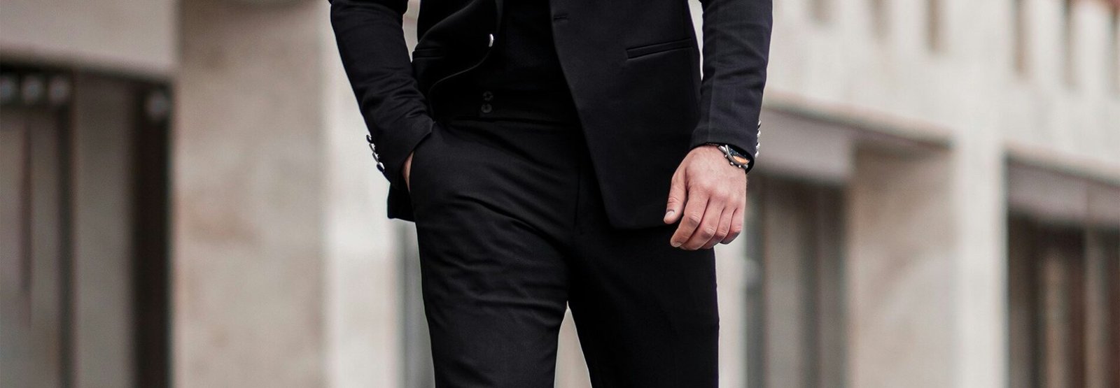 homme en veste de costume noir et pantalon noir debout sur un sol en beton gris pendant la journee