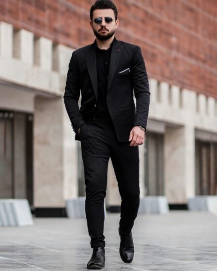 homme en veste de costume noir et pantalon noir debout sur un sol en beton gris pendant la journee